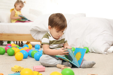 Wall Mural - Cute little boy with book playing on floor while girl sitting on bed. Children's development