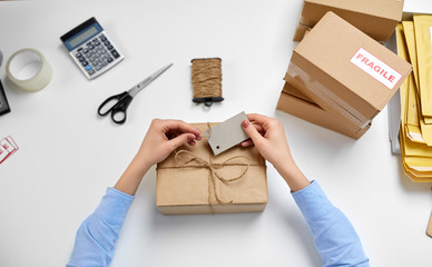 delivery, mail service, people and shipment concept - female hands tying name tag to parcel box at post office