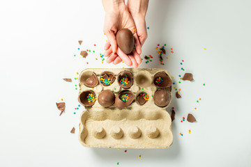 Wall Mural - Female hand takes or holds chocolate eggs and multi-colored sweet candy decorations from a tray on a light background. Easter concept, easter treats, bunny. Banner. Flat lay, top view