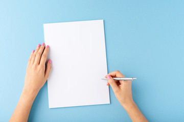 overhead shot of female hands writing with pen over empty white sheet of paper on blue background