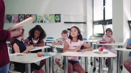 Poster - Teacher among small school children on the lesson, explaining.