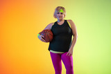 Fototapeta Młodzieżowe - Young caucasian plus size female model's training on gradient orange background in neon light. Doing workout exercises with the ball. Concept of sport, healthy lifestyle, body positive, equality.