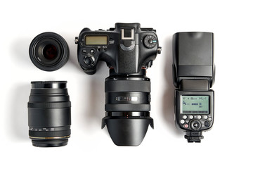 top view of modern digital camera equipment - DSLR with attached zoom lens and hood, lenses and external flashlight on white background