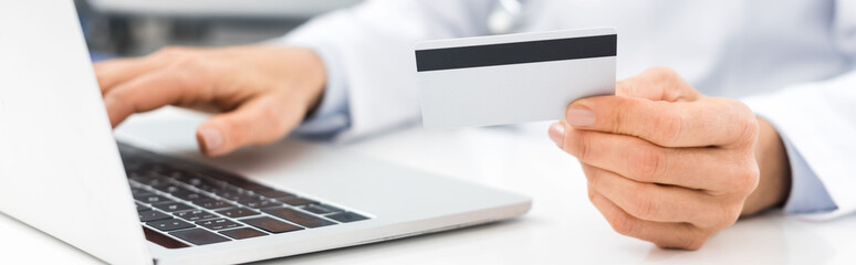 Wall Mural - panoramic shot of doctor using laptop and credit card in clinic