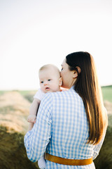 a young mother in a blue checked dress stands with her back to a small child looking at the camera o