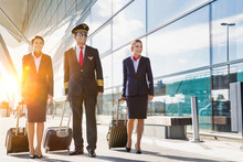 Mature Pilot With Young Beautiful Flight Attendants Walking In Airport