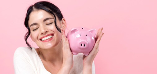Wall Mural - Young woman with a piggy bank on a pink background