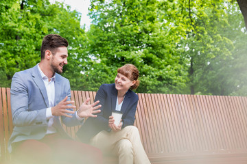 Wall Mural - Portrait of handsome businessman gesturing and talking to businesswoman while sitting on bench during office break