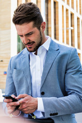 Wall Mural - Young handsome businessman using smartphone against office building