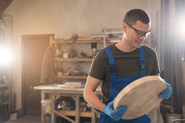 Poster - Professional carpenter with round piece of wood in workshop