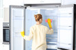 Woman in rubber gloves cleaning empty refrigerator at home, back view