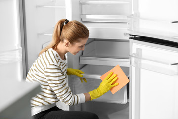 Wall Mural - Woman in rubber gloves cleaning empty refrigerator with rag at home