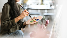 Cropped Image Of Young Beautiful Artist Girl Sitting In Front The Drawing Canvas While Painting An Oil Color At The Modern Studio. Beautiful Artist And Gallery Studio Concept.