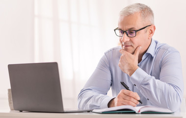 Senior man using laptop at home and writing