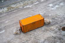 Vue De Dessus D'un Container En Acier Isolé Peint En Orange Vif. C'est Un Vieux Conteneur Rouillé Placé Sur Un Terrain. Deux Gros Rochers Bloquent Les Portes.