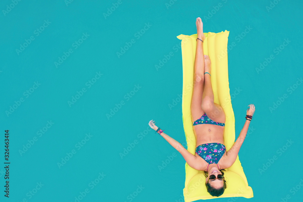 Woman in bikini on the inflatable yellow mattress in the swimming pool ...