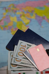 Two passports, one hundred dollar bills and bank cards. Against the background of a world map. Silhouettes of continents are visible.