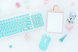 Fototapeta Kwiaty - Computer mouse and keyboard in mint white, pink clipboard, paper clip, candle, alarm clock, pink paper flower on a white table. Flat lay, top view..