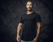 Gorgeous, adult, fit muscular caucasian man coach posing for a photoshoot in a dark studio under the spotlight wearing sportswear, showing his muscles looking calm and kind