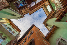 Rovereto, Italy Street Blue Sky In Small Historic Medieval Town Village In Trento Looking Up Low Angle Vertical View During Sunny Summer Day Multicolored Colorful Painted Walls And Balcony