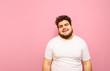 © bodnarphoto - Portrait of a funny overweight guy on a pink background, wearing a white t-shirt and beard, looking into the camera and smiling. Positive fat guy isolated on pink background. Copy space