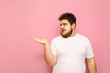 © bodnarphoto - Surprised guy with overweight, curly hair and a beard holds copy space in his hands and looks at the shocked advertising space. Funny charismatic fat man and a place left empty.