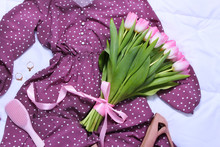 Close Up Of Purple Polka Dot Midi Dress, Beige High Heel Shoes,hair Brush,bouquet Of Pink Tulips And Accessories On Bed On White Sheet. Women's Stylish Spring Outfit. Trendy Clothes Collage.