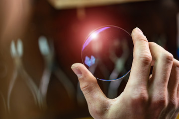 ophthalmologist hands showing a glass lens for spectacles. Blurred background. Ophtalmologist equipment. Vision correction concept. Closeup