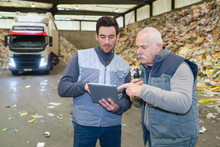 Two Male Workers Looking At Tablet Pc In Refuse Center