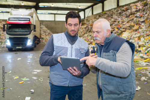 Fotografía two male workers looking at tablet pc in refuse center