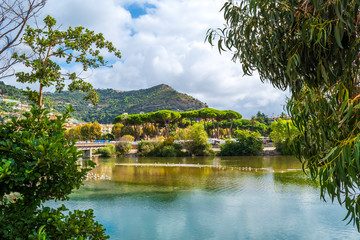 View through trees and across the Roya River of the italian hillside and village of Ventimiglia, Italy, on the coast of the Italian Riviera.