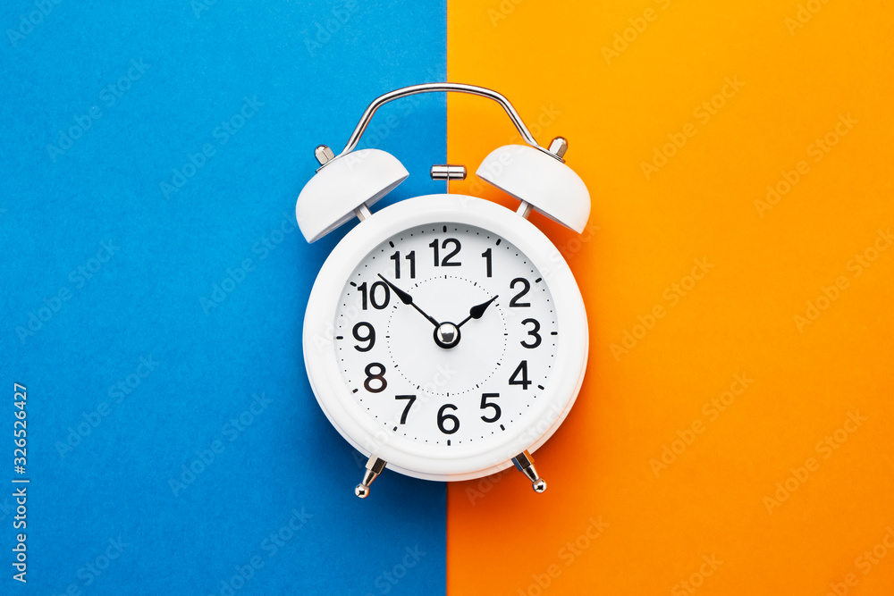 White vintage alarm clock on blue-orange background. Top view, copy space. Daylight saving concept. - obrazy, fototapety, plakaty 
