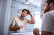© Graphicroyalty - Handsome young man touching his hair with hand and grooming in bathroom at home. White metrosexual man worried for hair loss and looking at mirror his receding hairline.