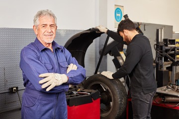 Car master in his auto repair shop and apprentice