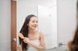 © makistock - Happy attractive young woman combing wet hair with comb in bathroom after shower at home. Hair care and healthy hair