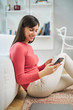 © nenadaksic - Young smiling woman sitting at home on the floor and using smart phone.