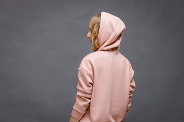 Wall Mural - A beautiful young girl stands with her back and turns around in a pink hoodie on a gray background.