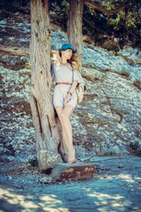 Wall Mural - Beautiful girl model in a gray summer dress and a fashionable blue spotted hat barefoot near a tree