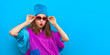 © LoopAll - Cool teenager. Fashionable DJ girl in colorful trendy jacket and vintage retro sunglasses enjoys style of 80s � 90s vibes. Teenager Girl at disco party. Young fashion model on blue color background.