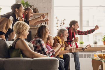 Excited, happy big family watching football, soccer match on the couch at home. Fans emotional cheering for favourite national team. Having fun from grandparent to children. Sport, TV, championship.