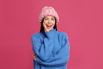 Poster - Young woman wearing warm sweater and hat on crimson background. Winter season