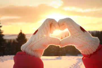 Wall Mural - Woman making heart with hands outdoors at sunset, closeup. Winter vacation