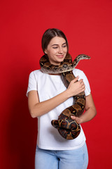 Canvas Print - Young woman with boa constrictor on red background. Exotic pet