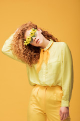 stylish redhead woman in sunglasses with flowers posing isolated on yellow