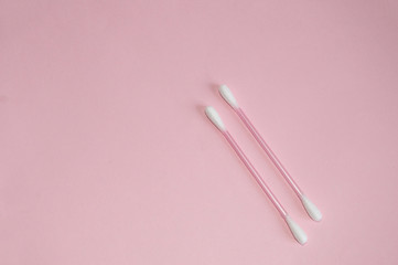 Top view, flat lay, two pink plastic cotton swabs neatly arranged on a pink background, the concept of cleanliness and hygiene