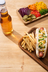 Wall Mural - delicious hot dog near board with sliced vegetables, beer and french fries on wooden table