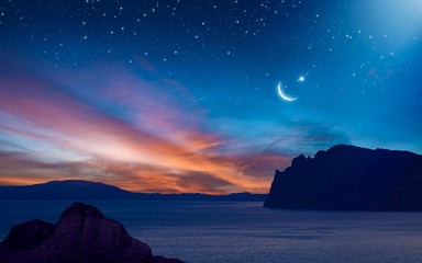 Wall Mural - Ramadan background with crescent, stars and glowing clouds with ray from skies above mountains and sea. Month of Ramadan is that in which was revealed Quran.