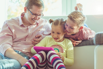 Wall Mural - Happy young handsome father having fun with his two cute children playing with tablet