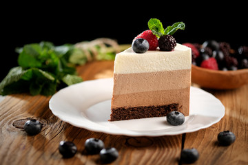 Piece of light mousse cake with fruits on on wooden surface. Mousse cake recipe for three chocolates.