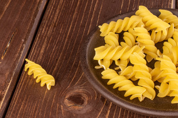 Wall Mural - Lot of whole yellow pasta fusilli with brown ceramic coaster on brown wood